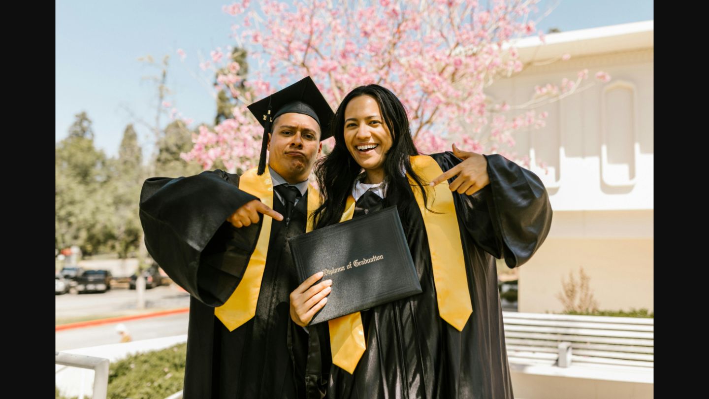 Two graduates smiling and pointing at a diploma